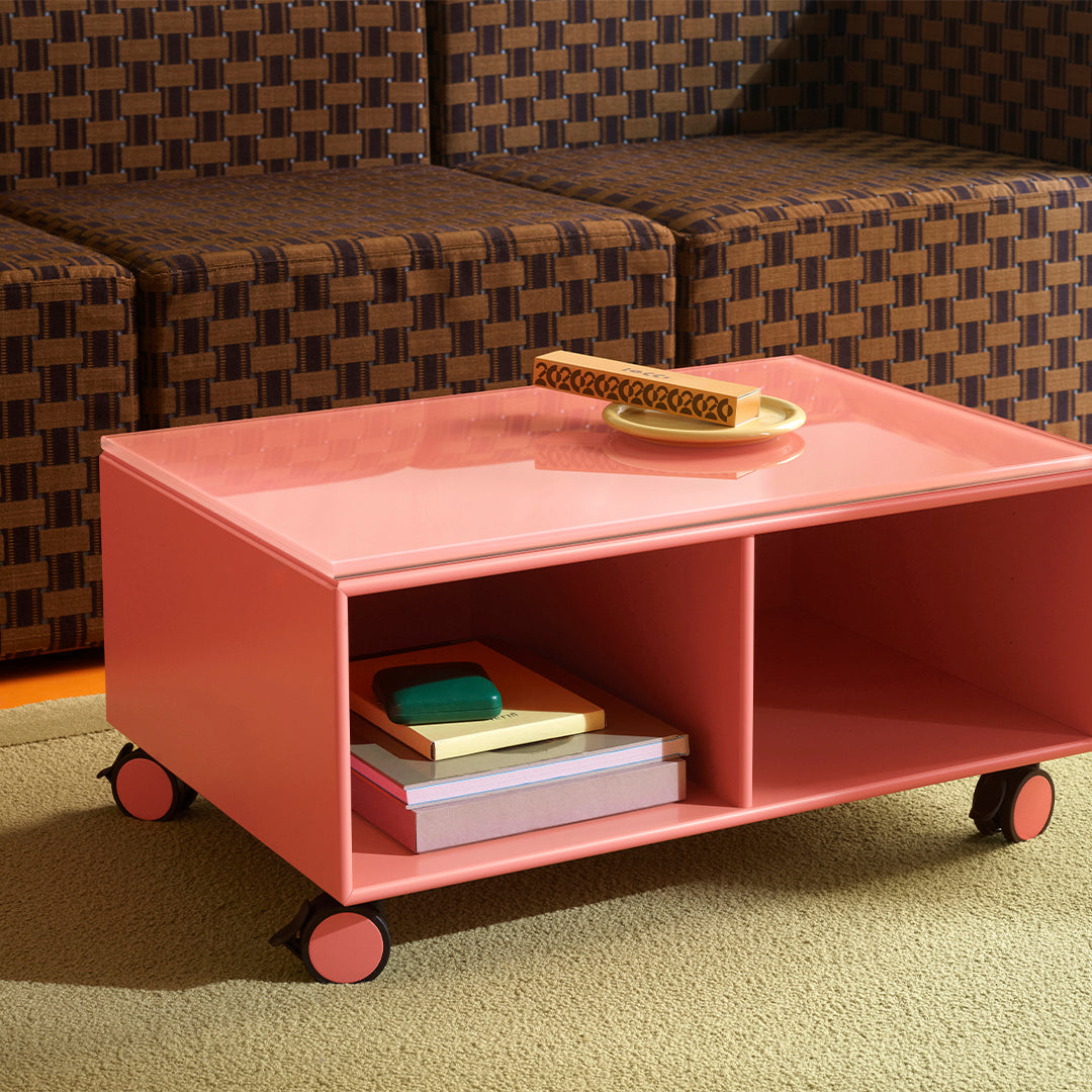 "Pink coffee table with smooth finish, featuring vibrant colored books and a textured brown patterned couch."