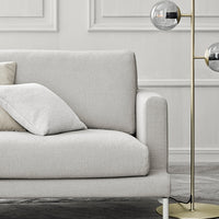 Stylish light gray sofa with soft cushions, complementing gold floor lamp and neutral backdrop for a modern look.