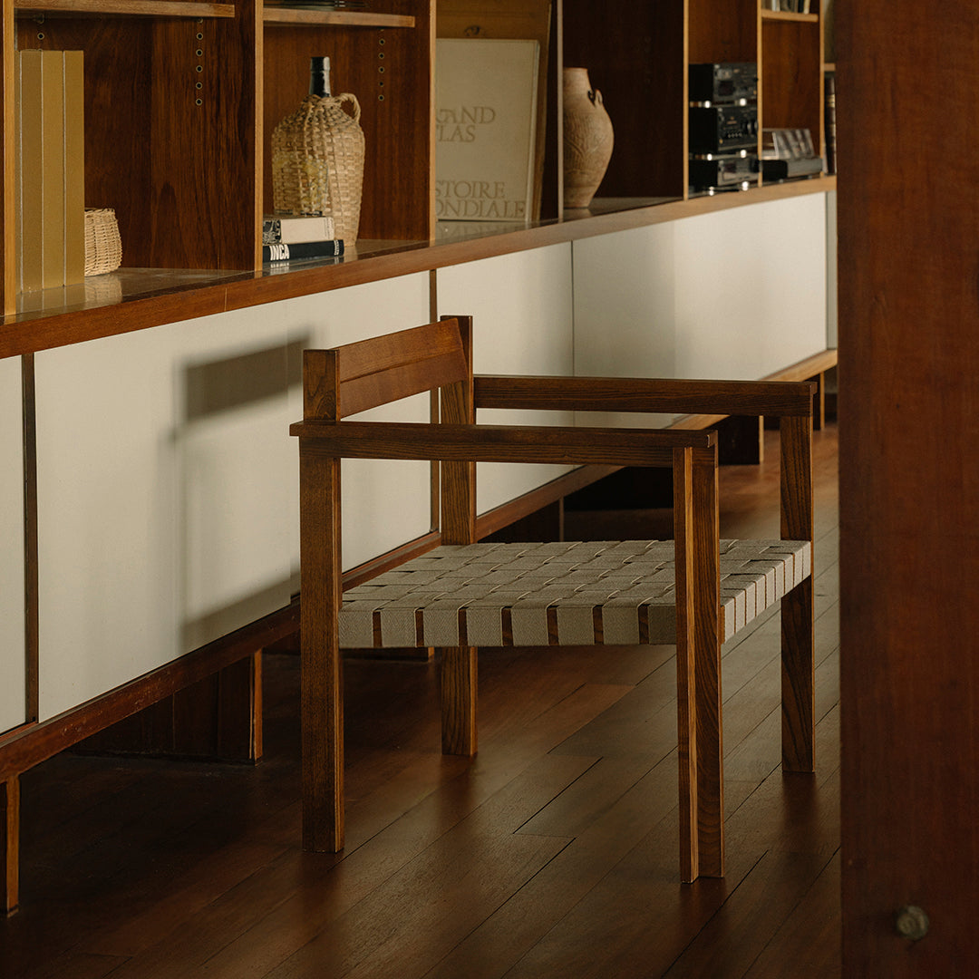 "Wooden chair with a natural finish and woven gray and white striped seat, set against a minimalist backdrop."