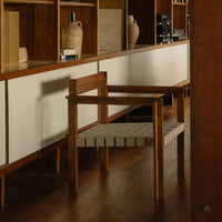 "Wooden chair with a natural finish and woven gray and white striped seat, set against a minimalist backdrop."