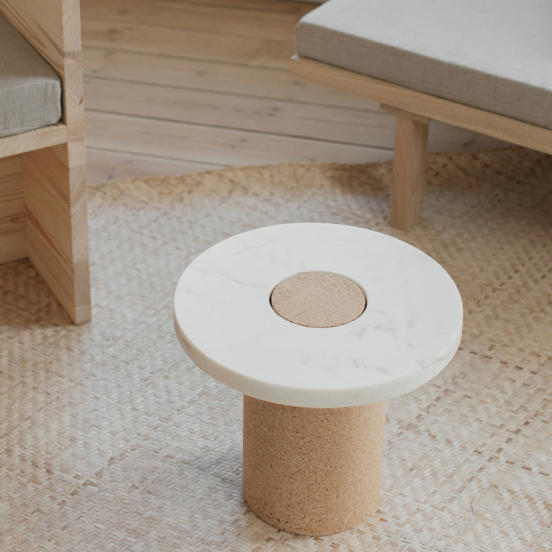 Round white marble table with a cork base, set on a woven natural fiber rug, creating a minimalist and modern look.