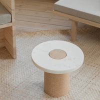 Round white marble table with a cork base, set on a woven natural fiber rug, creating a minimalist and modern look.