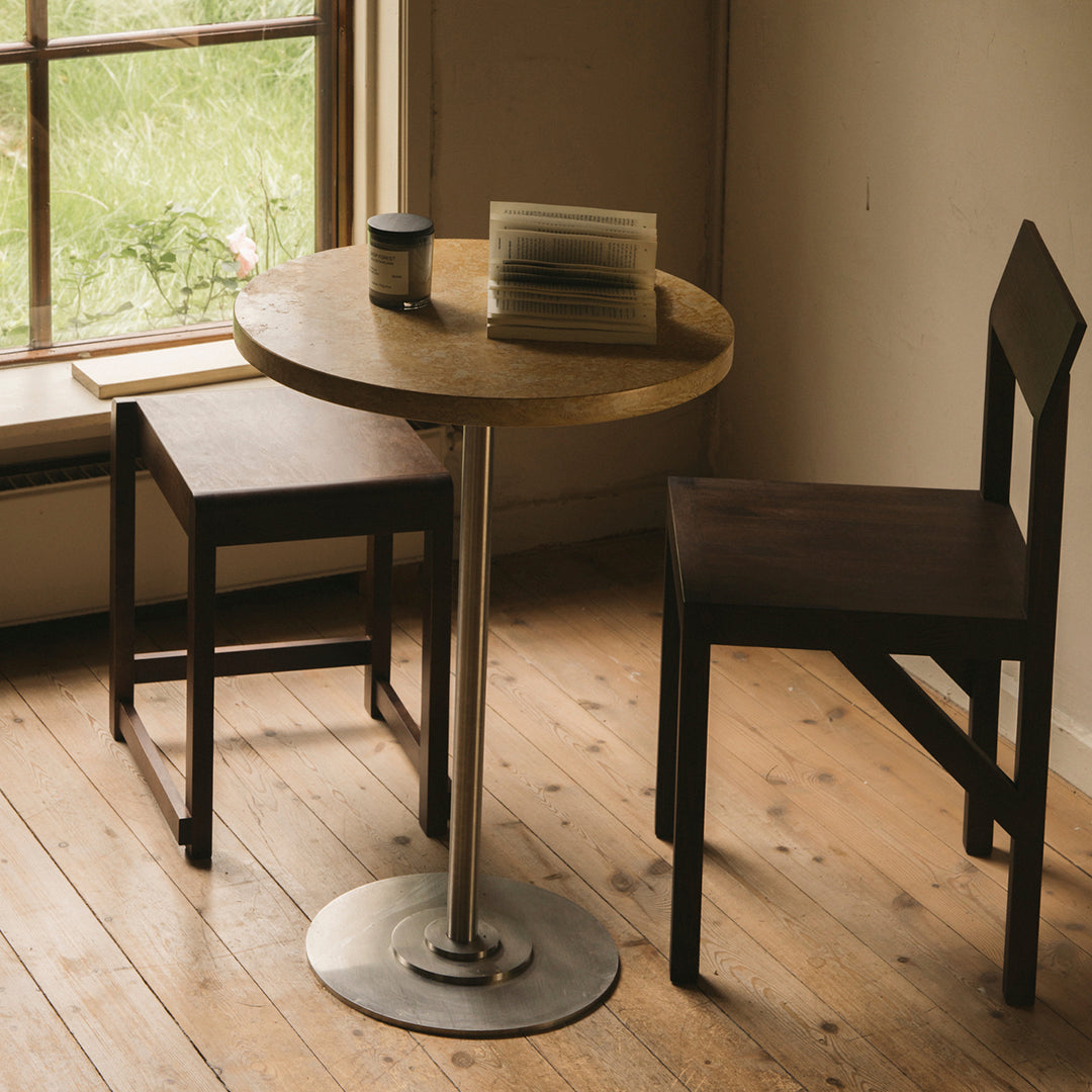 Round wooden table with a light finish, paired with two dark wooden chairs on a natural wood floor.