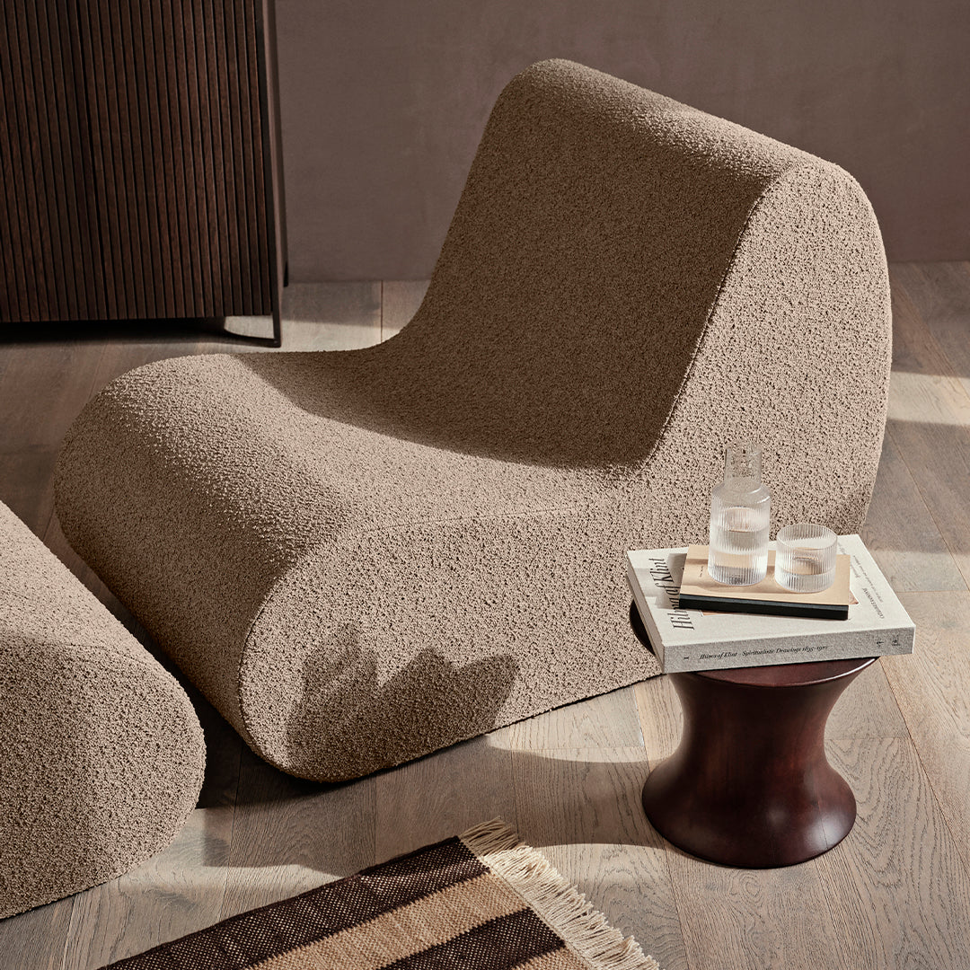 Textured beige lounge chair with rounded shape, complementing a minimalist decor featuring natural wood and muted tones.