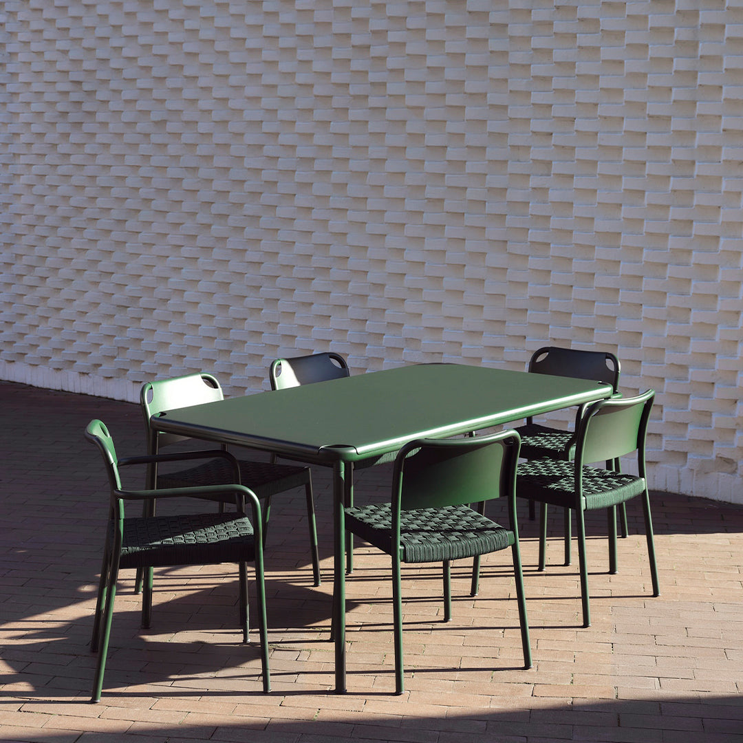 Green outdoor dining table and chairs set against a textured white wall. Modern design with sleek lines and bold colors.