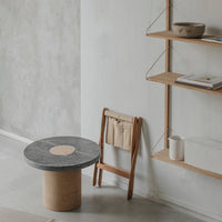 Round black and beige stone table with a simple, natural wood chair against a minimalist gray wall.
