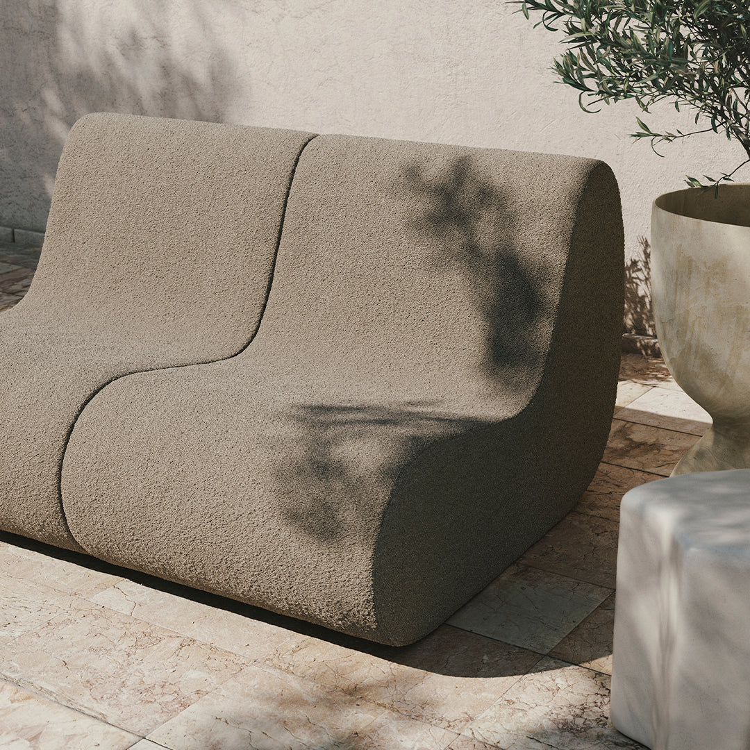 Textured taupe sofa with a modern curved design, complemented by natural stone and greenery backdrop.