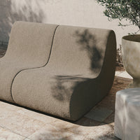Textured taupe sofa with a modern curved design, complemented by natural stone and greenery backdrop.