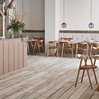 Light wood floor with warm tones, pastel pink bar, and soft gray upholstered seating create a cozy, modern atmosphere.