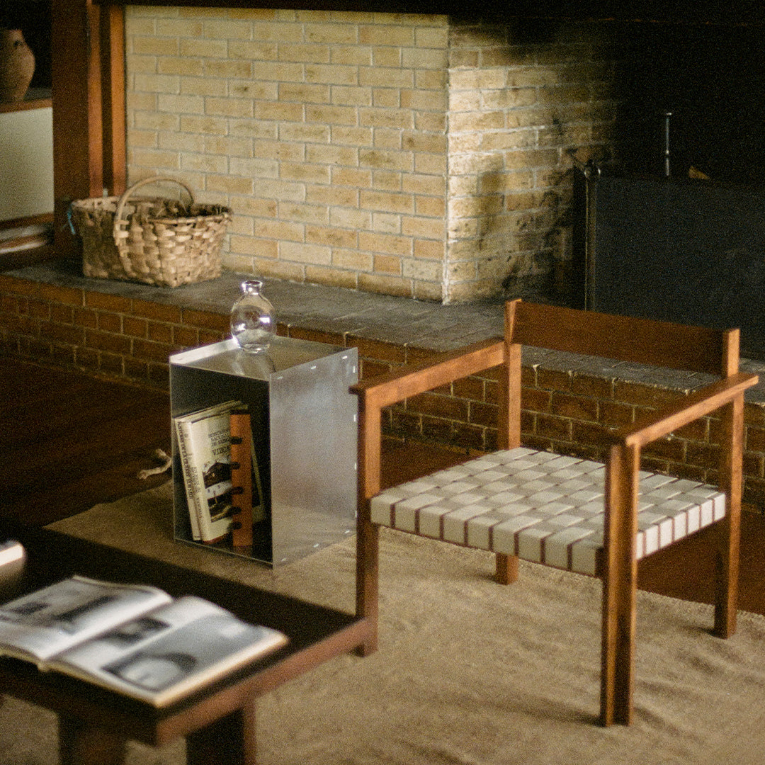 Wooden chair with a geometric black and white woven seat, complementing earthy tones of the room decor and brick fireplace.