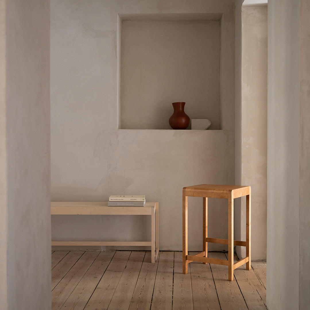 Natural wood bench and stool against a muted beige wall, featuring subtle textures and organic shapes.