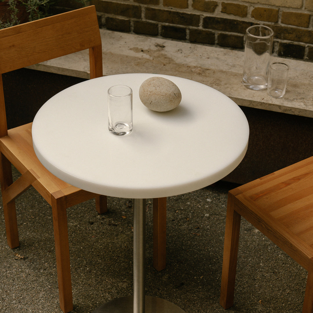Round white table with a smooth surface, paired with wooden chairs featuring light and dark wood patterns.