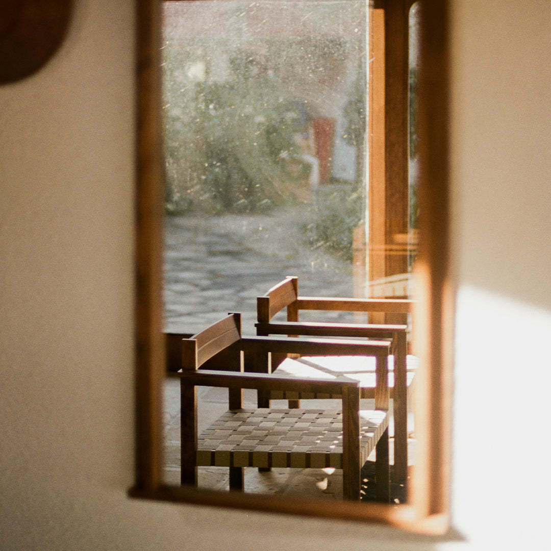 Wooden chairs with a woven pattern, bathed in natural light, framed by a warm-toned mirror reflection.