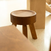 Brown wooden stool with a smooth, circular seat and three tapered legs, showcasing natural wood grain patterns.
