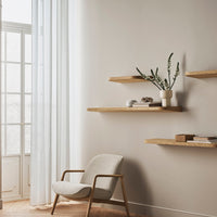 Modern beige wall with light wood shelves, soft gray chair, and sheer white curtains, creating a calm and minimalistic aesthetic.