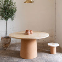 Natural beige round table with a textured surface, complemented by a minimalist white stool and earthy terracotta pots.