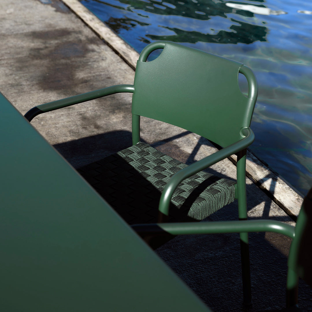 Green chair with a checkerboard-patterned seat next to a pool, set against a textured concrete surface.