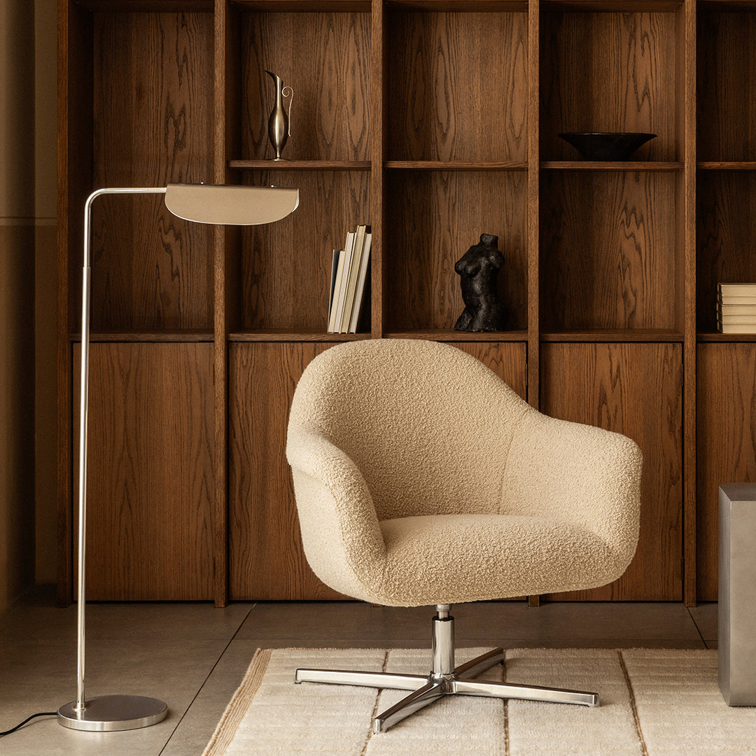 Beige textured chair with silver metallic base, set against rich wooden bookshelf backdrop. Modern and cozy aesthetic.