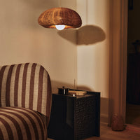 Brown striped sofa with a natural woven pendant light, black textured side table, warm ambient lighting.