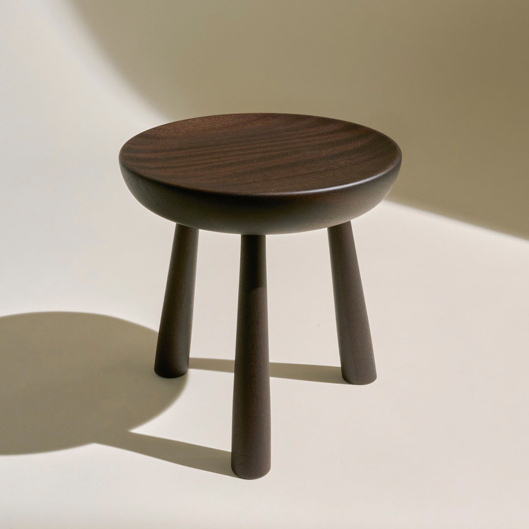 Dark brown wooden stool with a smooth, round top and tapered legs, featuring a natural wood grain pattern.