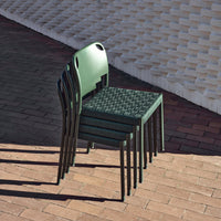 Stacked green chairs with a textured pattern against a warm-toned brick background.