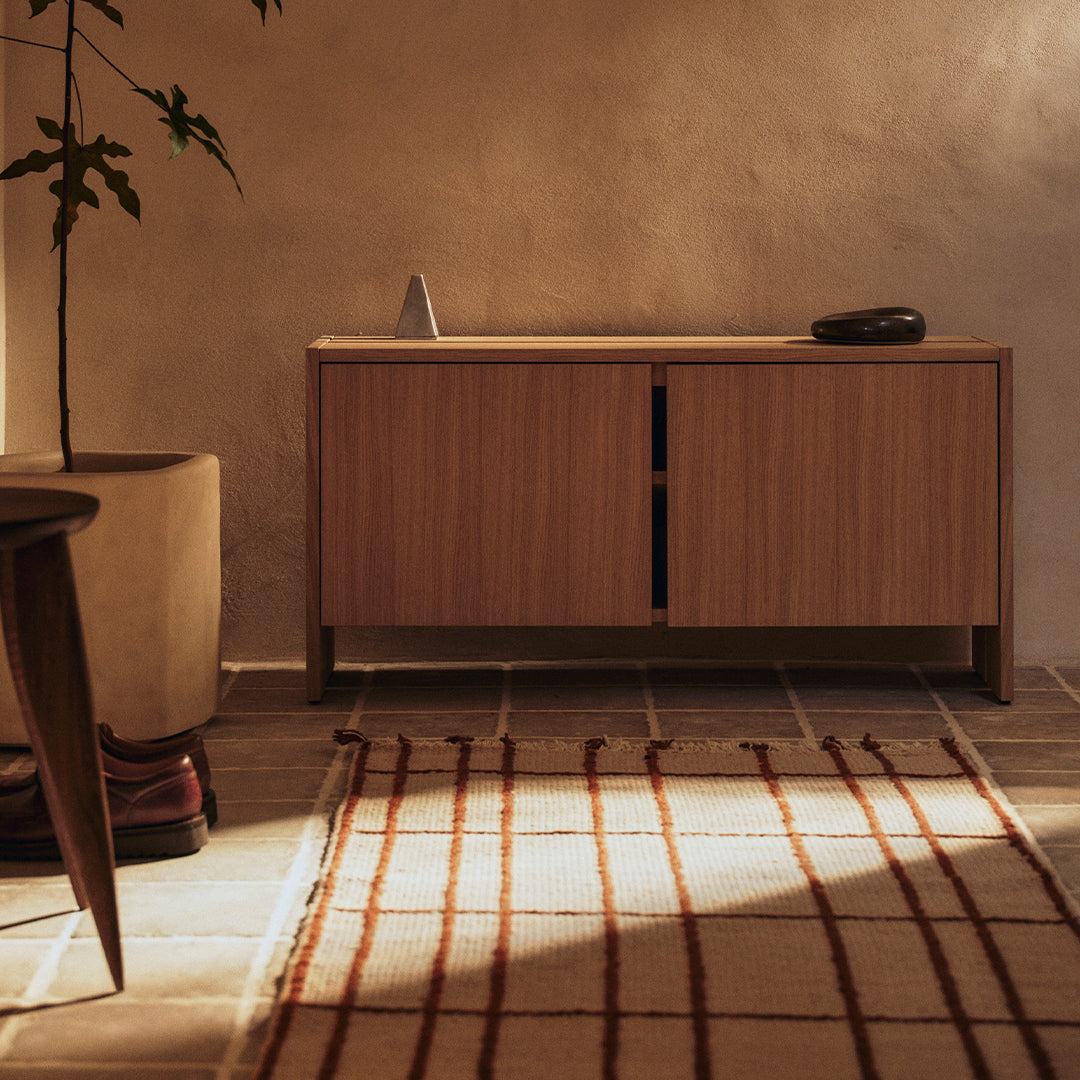 Wooden sideboard in warm brown with a minimalist design, complemented by a cream rug featuring red geometric lines.