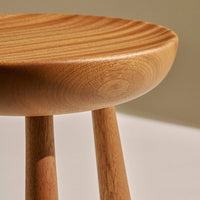 Natural wood stool with light brown tones and a smooth, rounded top featuring subtle, wavy grain patterns.