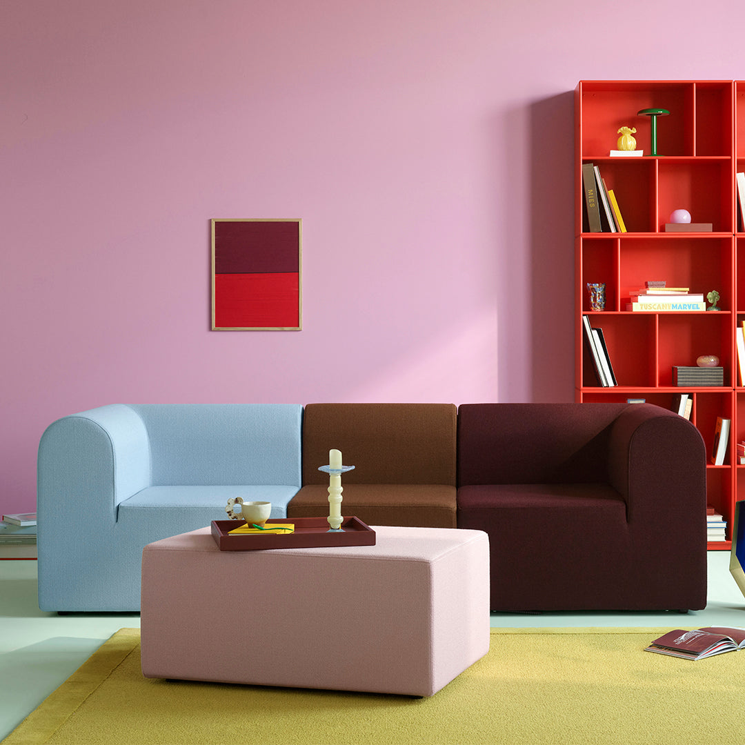Multicolored sofa with blue, brown, and burgundy sections; pink coffee table and yellow area rug against a pink wall.