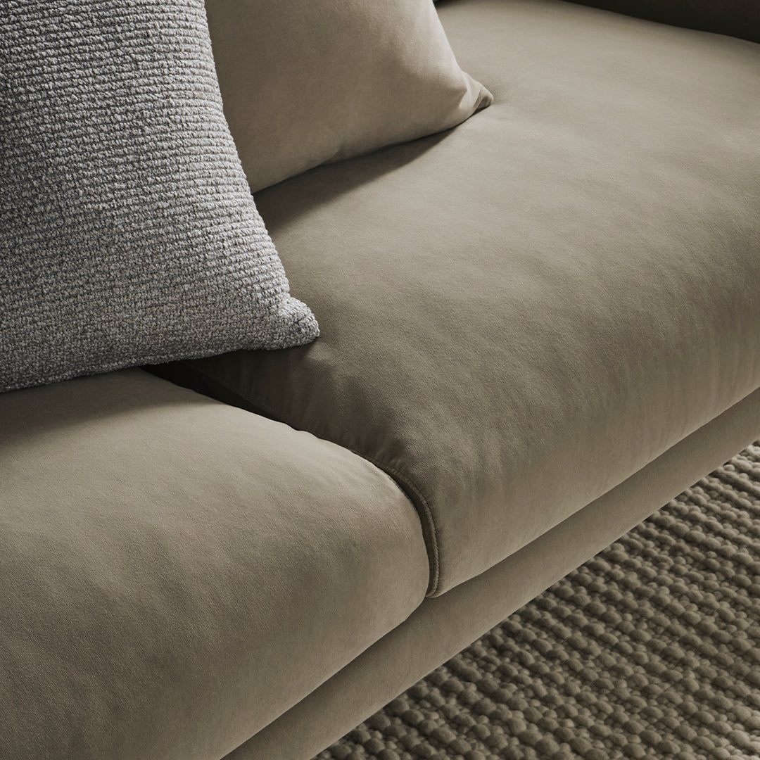 "Soft taupe sofa with textured throw pillow, complemented by a woven gray rug."