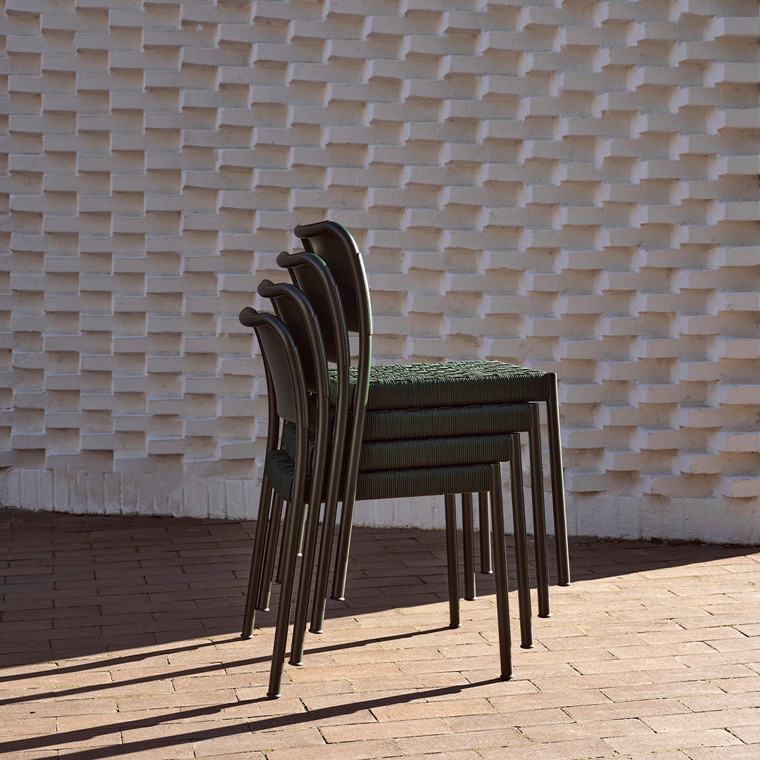 Stacked chairs featuring a dark green pattern against a textured white brick background. Shadows create depth.