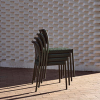 Stacked chairs featuring a dark green pattern against a textured white brick background. Shadows create depth.