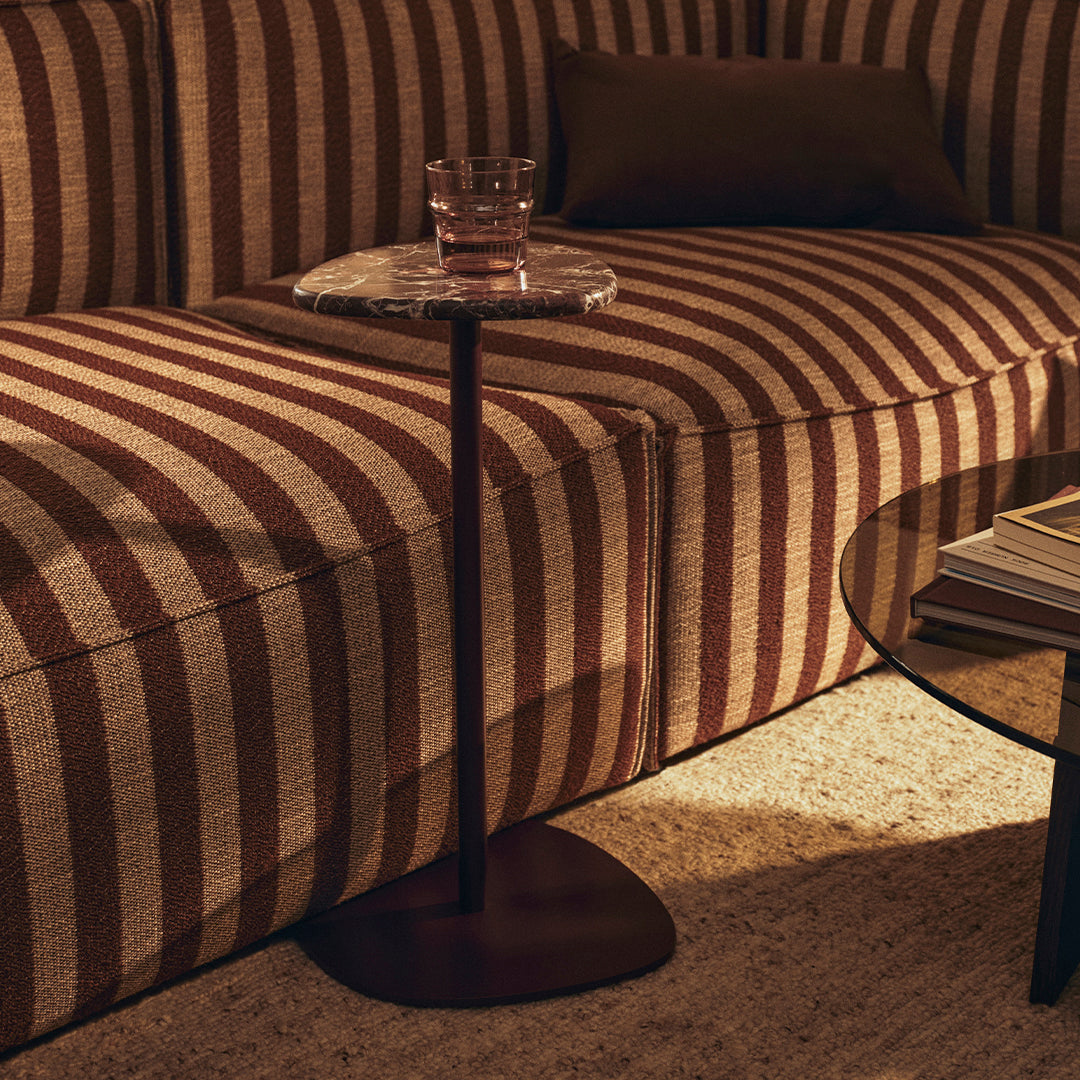 Brown and cream striped fabric sofa with a sleek black side table, featuring a round marble top. Cozy and stylish.