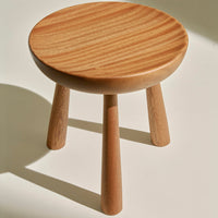 Natural wood stool with a smooth, round top and tapered legs, showcasing a warm, light brown finish and subtle grain patterns.
