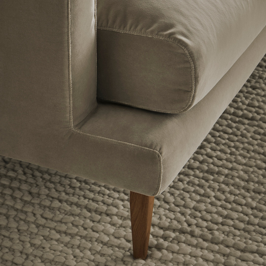 Soft beige velvet couch with a clean, modern design and natural wood legs, resting on a textured neutral rug.