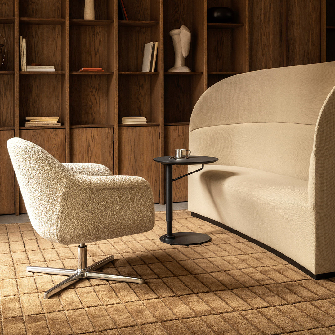 Cream-colored boucle armchair with a smooth beige sofa and a sleek black side table on a textured tan rug.