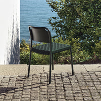 Black patio chair with a woven green seat against a natural outdoor backdrop by the water.