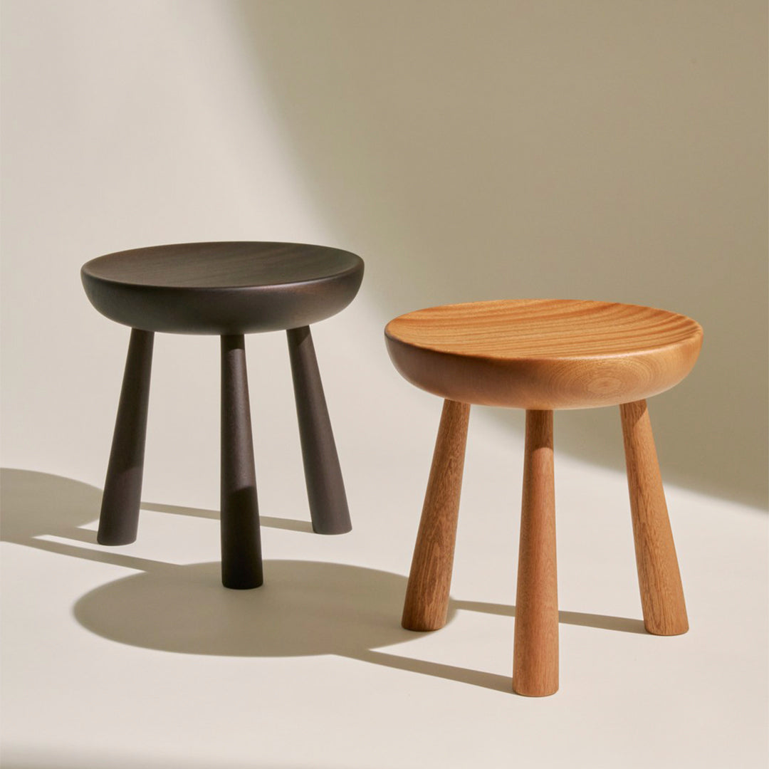 Two minimalist stools: one in matte black and the other in natural wood with a smooth finish and subtle grooves.