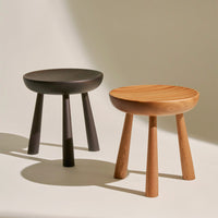 Two minimalist stools: one in matte black and the other in natural wood with a smooth finish and subtle grooves.