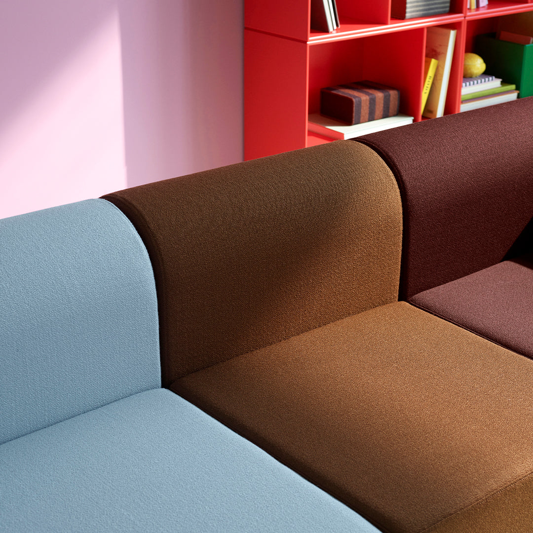Multicolored sectional sofa featuring soft blue, rich brown, and deep burgundy upholstery against a pastel pink background.