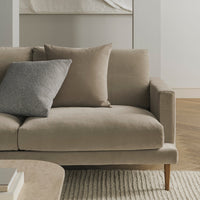 Light beige sofa with a textured gray pillow, featuring clean lines and a minimalist style on a light wood floor.