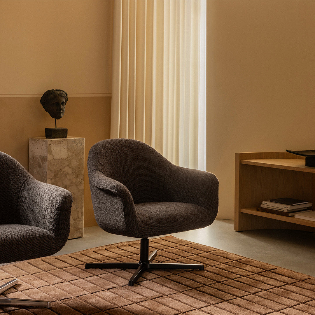 Contemporary dark gray swivel chairs on a textured beige rug, set against warm, neutral-toned walls.
