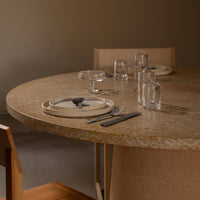 Round table with a textured, earthy-toned surface, complemented by neutral plates and clear glassware.
