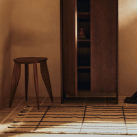 Wooden stool and cabinet against a warm beige background; striped rug with earth tones and neutral colors.