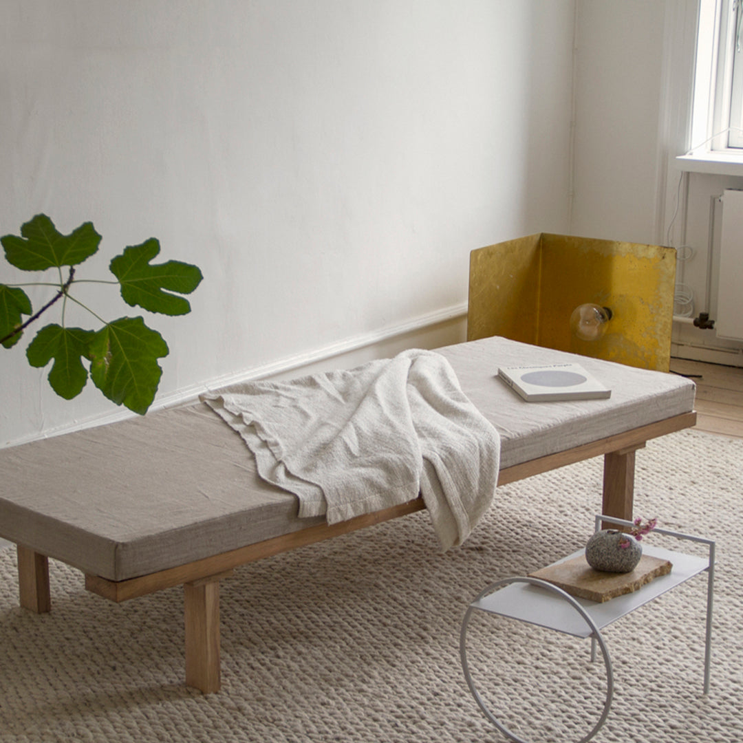 Neutral beige mattress with a textured pattern, accompanied by a cream throw and a minimalist white side table.