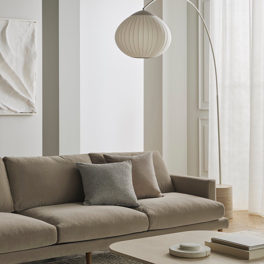 Neutral beige sofa with a gray accent pillow, surrounded by soft white walls and natural light. Modern minimalist aesthetic.