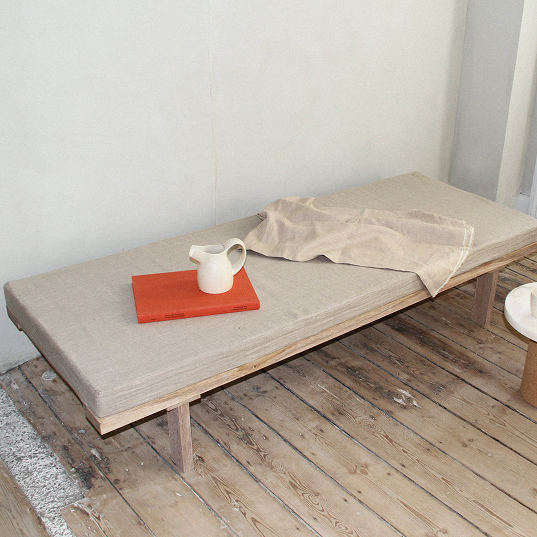 Neutral beige cushion on a wooden platform, paired with an orange accessory and soft linen drape.
