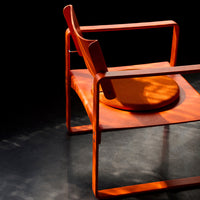 Bright orange chair with a sleek design, featuring a circular cushion, set against a dark background.