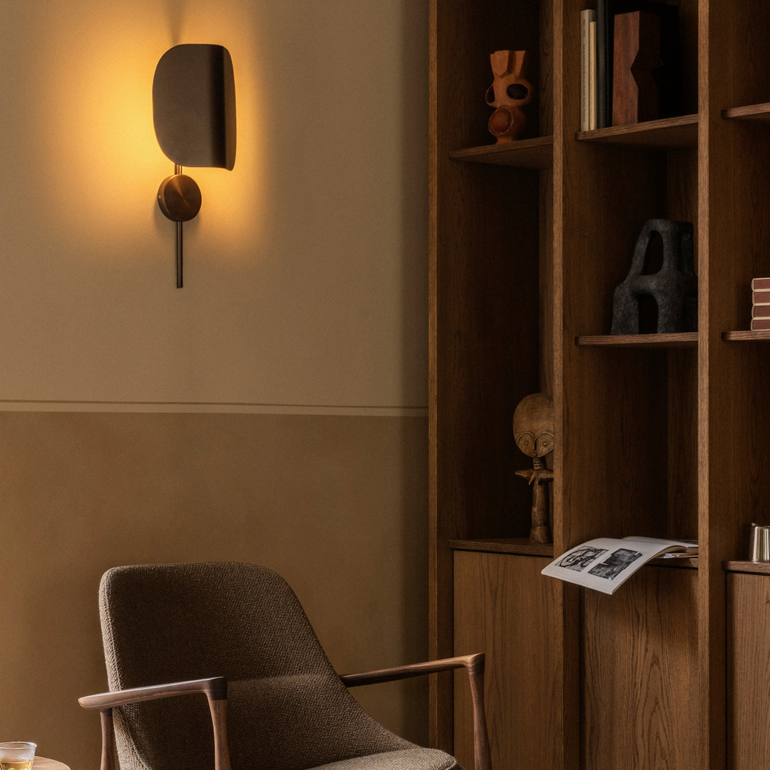 Warm beige walls with a stylish brown chair and dark wooden shelves featuring artistic decor and soft ambient lighting.