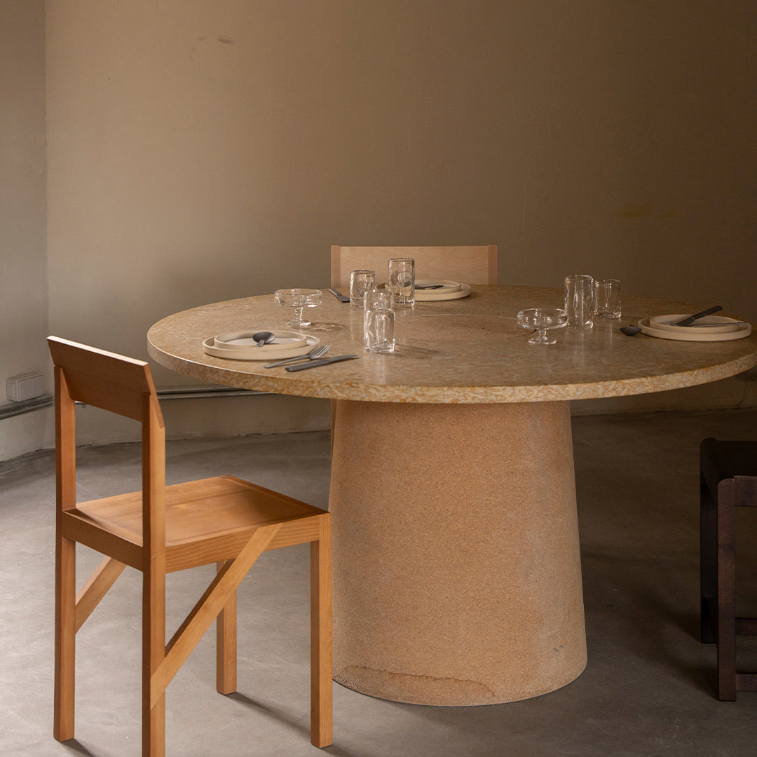 Round natural cork dining table with a smooth surface, paired with minimalist wooden chairs in a neutral-toned setting.