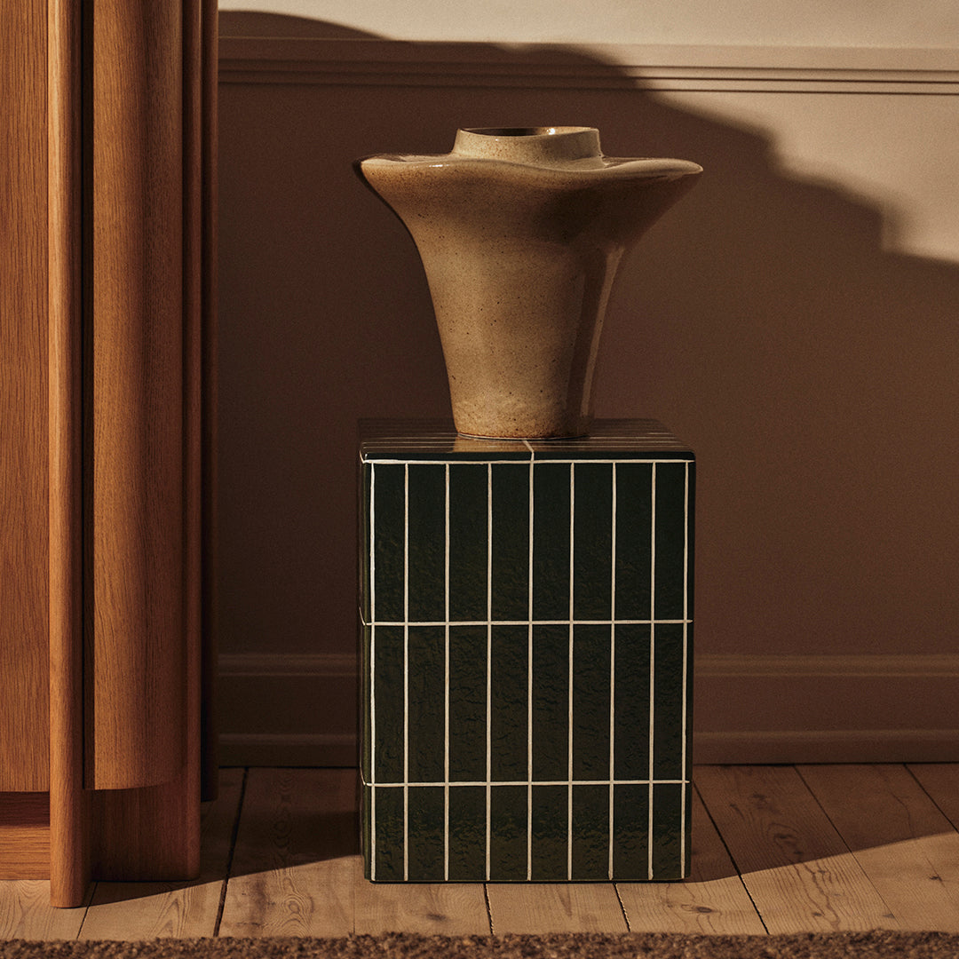 Terracotta vase atop a dark green and white striped pedestal, highlighting earthy tones and contemporary design.